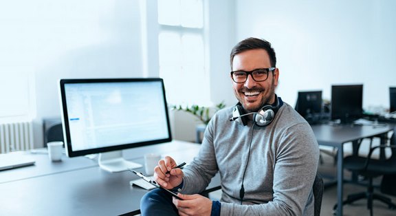 Freundlicher Kundensupport-Mitarbeiter mit Headset vor einem Computerbildschirm, symbolisiert dauerhafte Kundenbetreuung und Website-Optimierung.