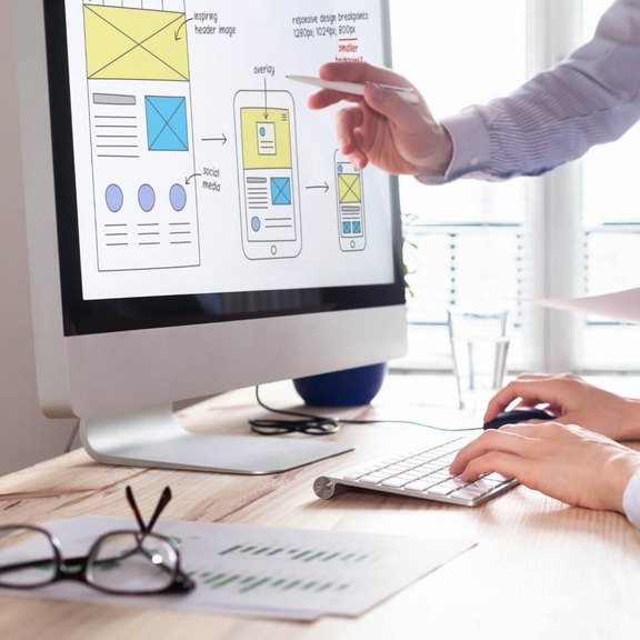 Zwei Fachleute optimieren das Layout einer Webseite auf einem Computerbildschirm, wobei die Schritte für responsives Design diskutiert werden.